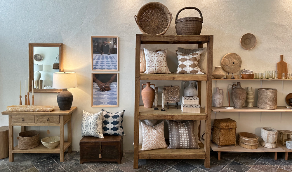 Interior of a home decor store showcasing a variety of items including pillows, pictures of artisans, terracotta vessels, shelving units, and glassware.