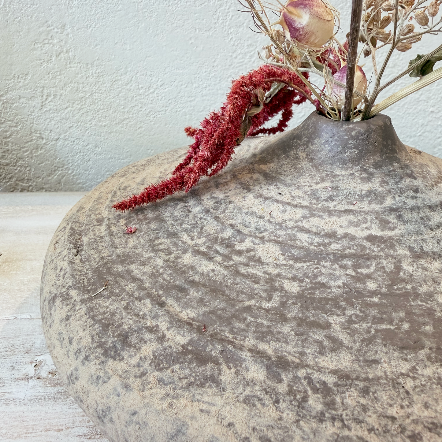 Decorative stone vase with dried flowers on a light wooden surface