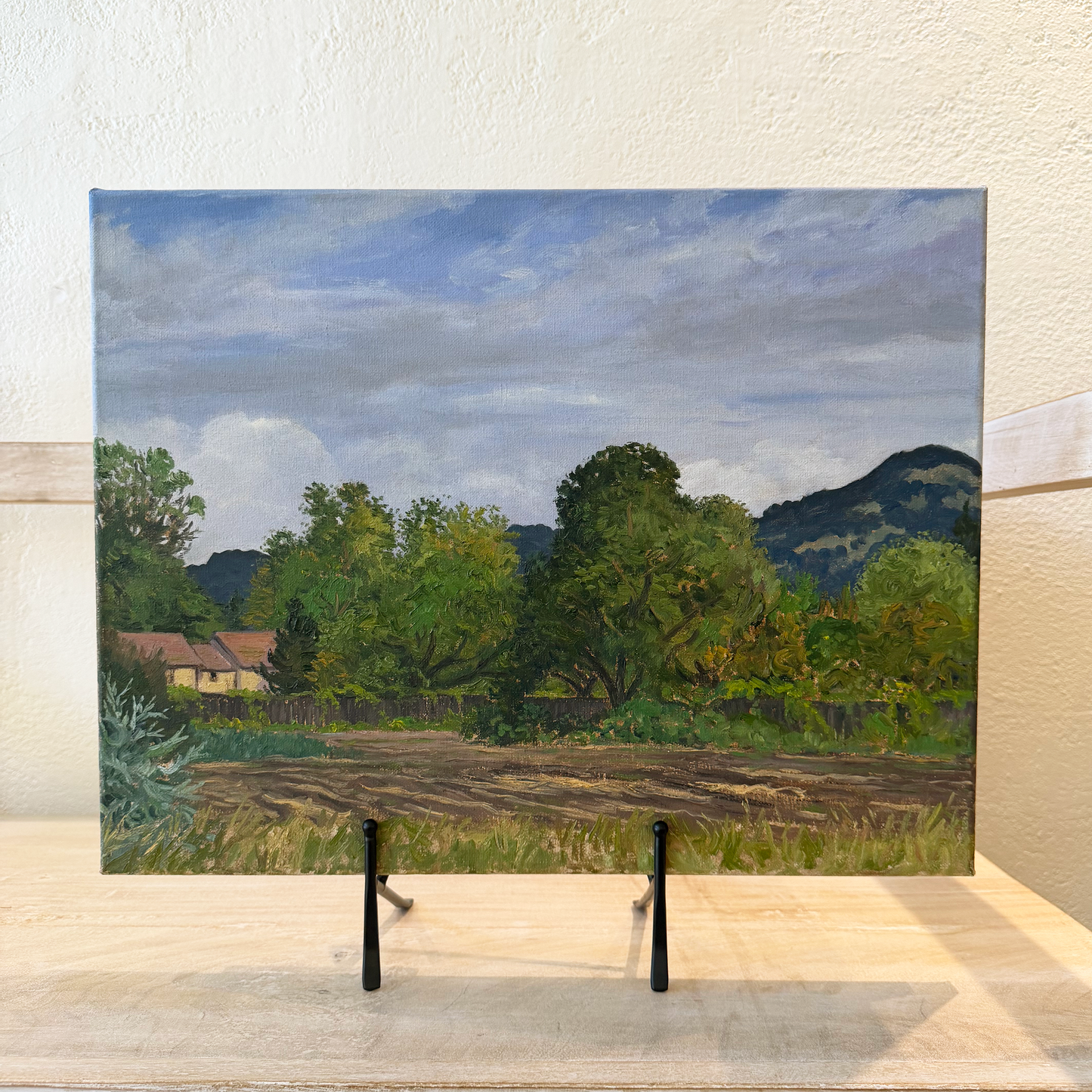 Painting of a landscape with trees and mountains on a stand.