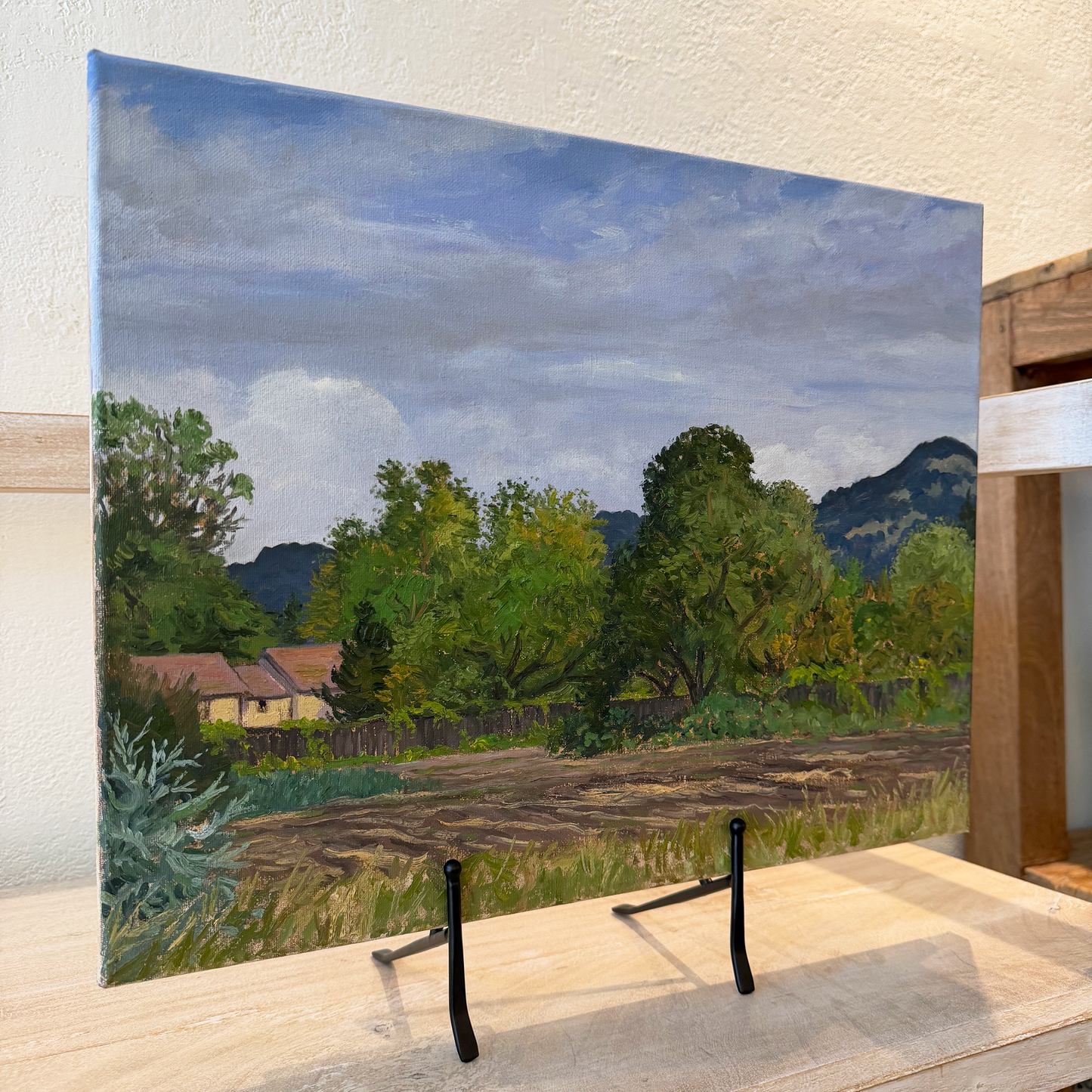 Painting of a landscape with trees and mountains on an easel.