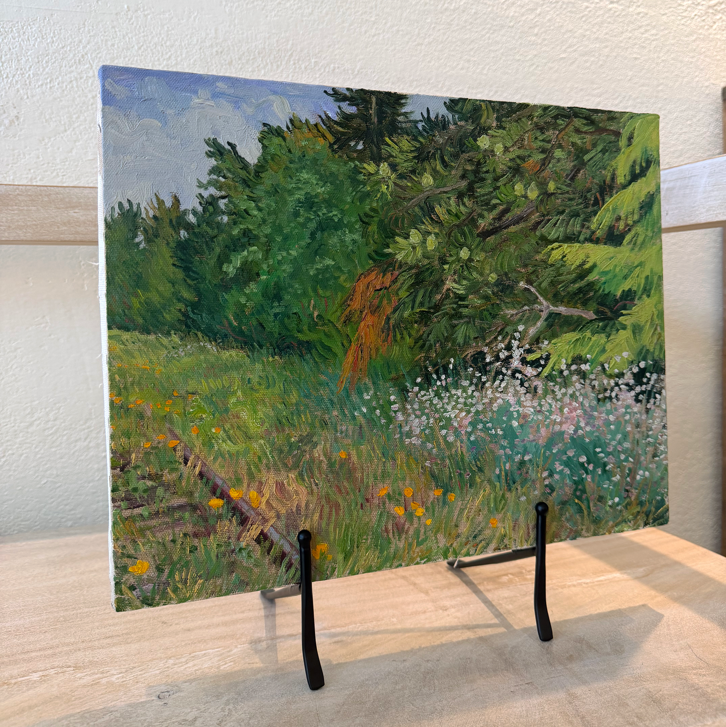 Framed artwork of a landscape with trees and grass on a wooden surface.