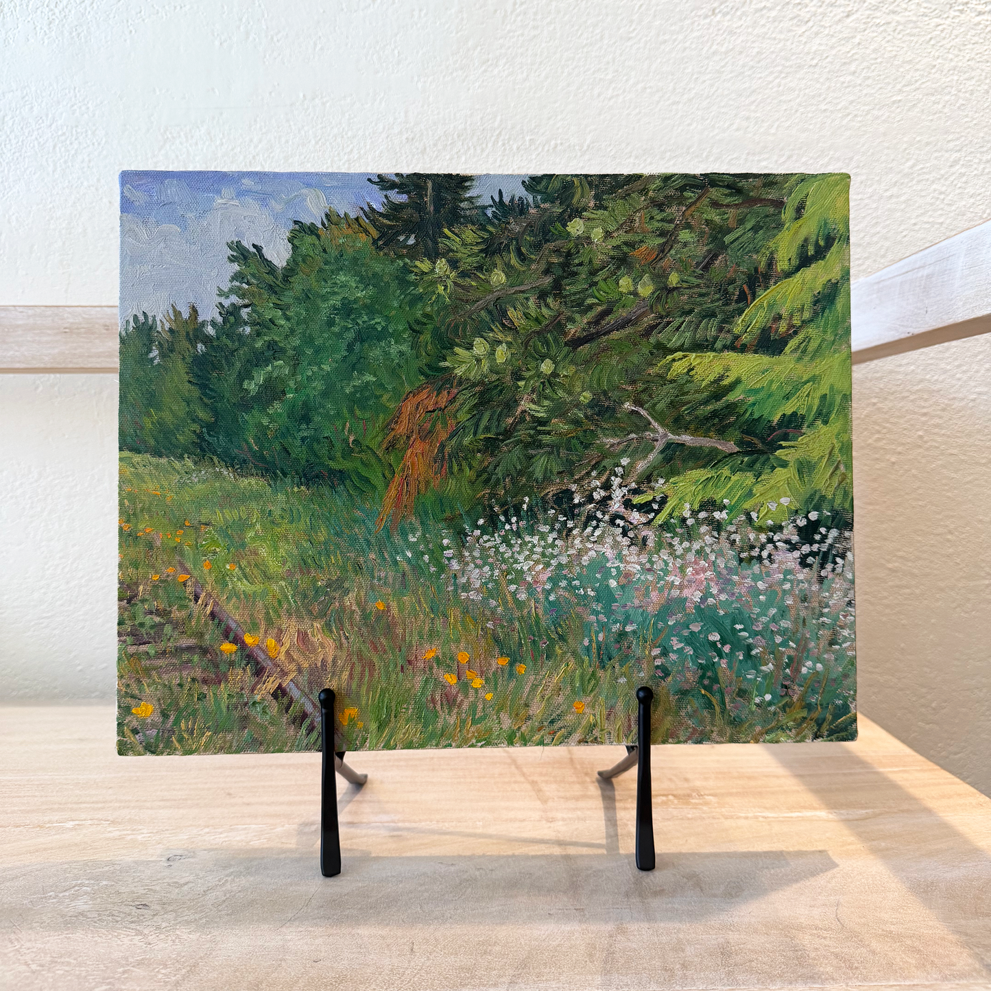 Painting of a natural landscape with trees and flowers on an easel.
