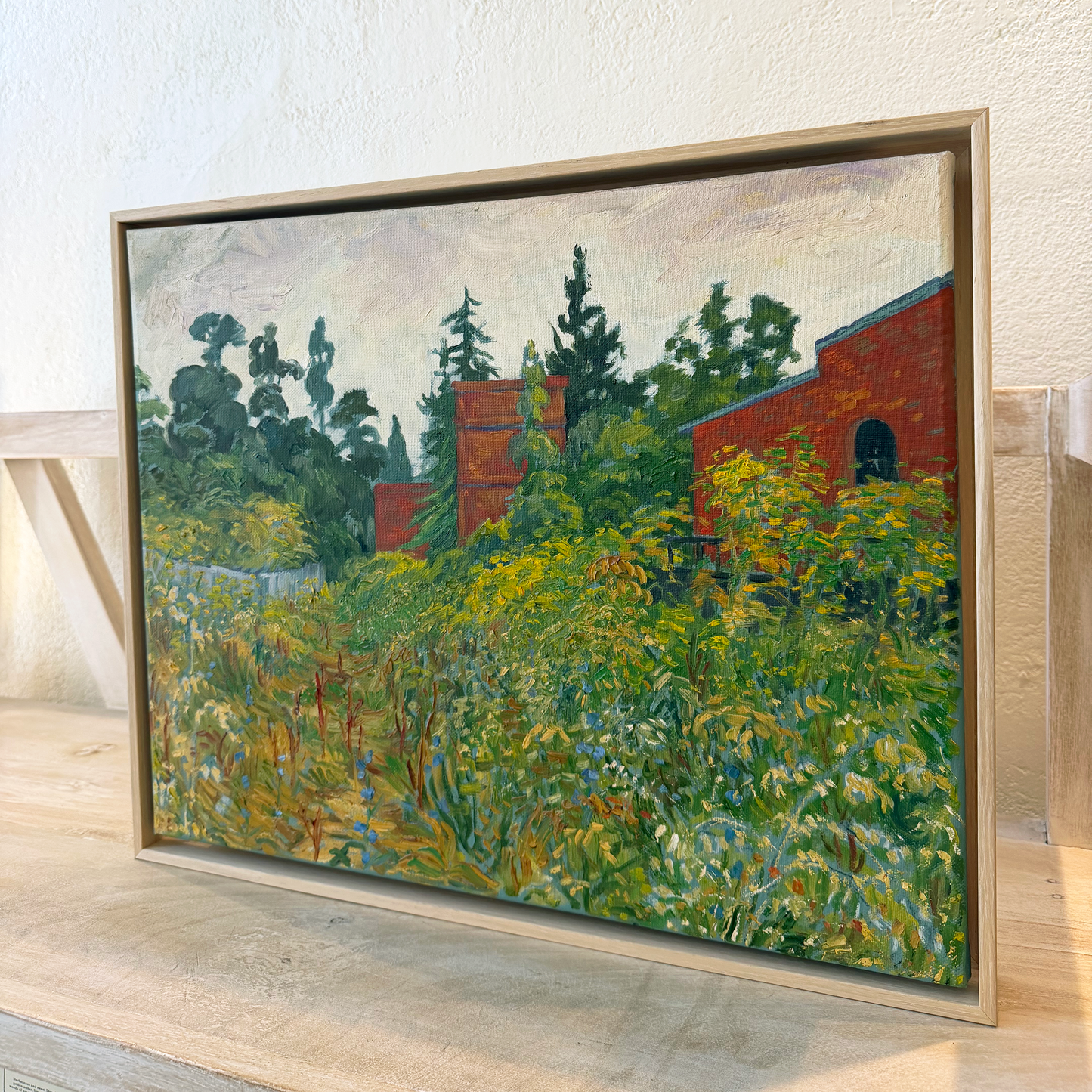Framed painting of a landscape with trees and a building on a wooden surface.