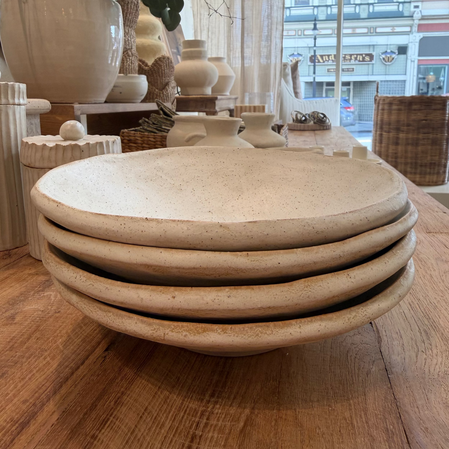 
                  
                    Stack of ceramic bowls on a wooden surface with decorative vases in the background.
                  
                