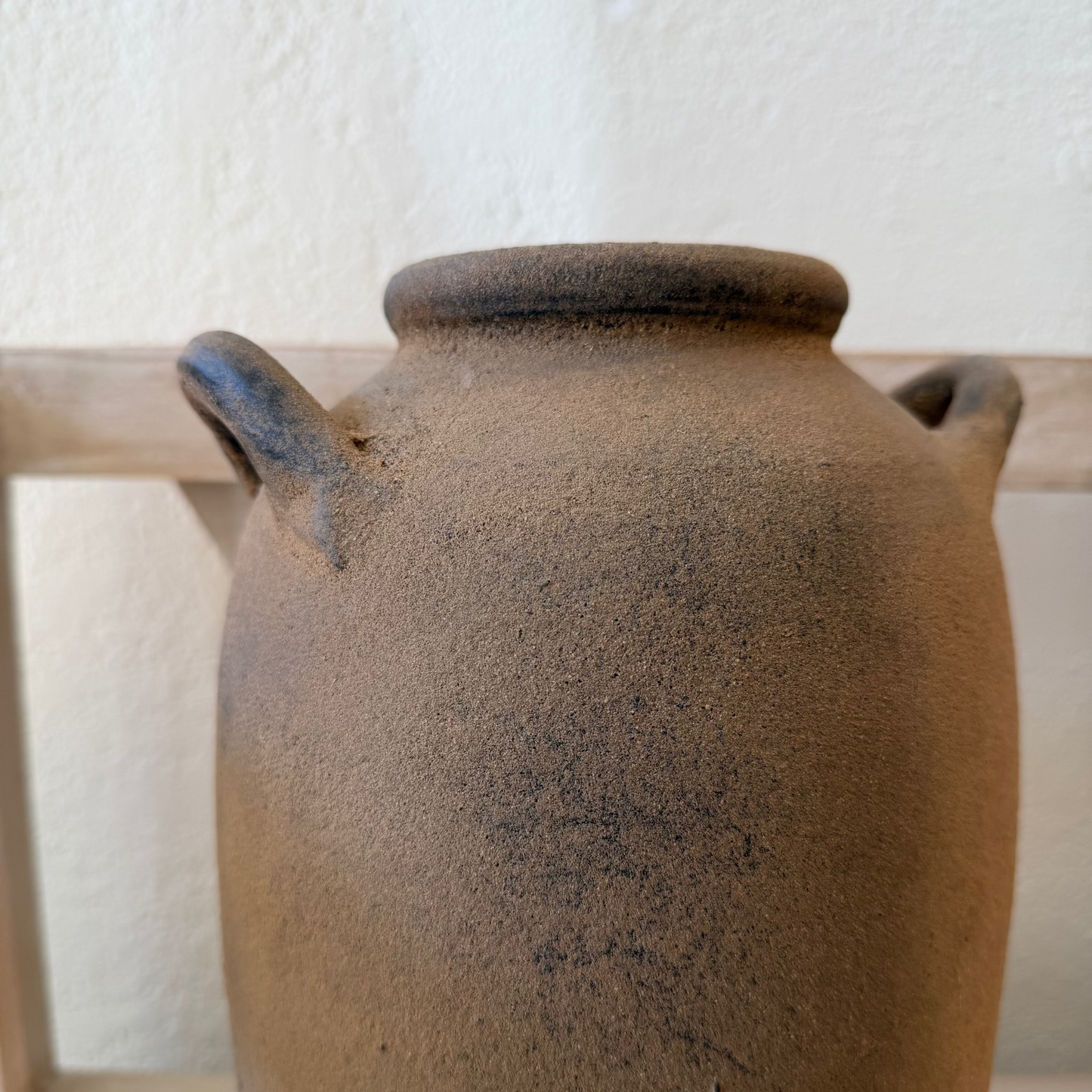 Brown ceramic jar with a textured surface on a wooden shelf.