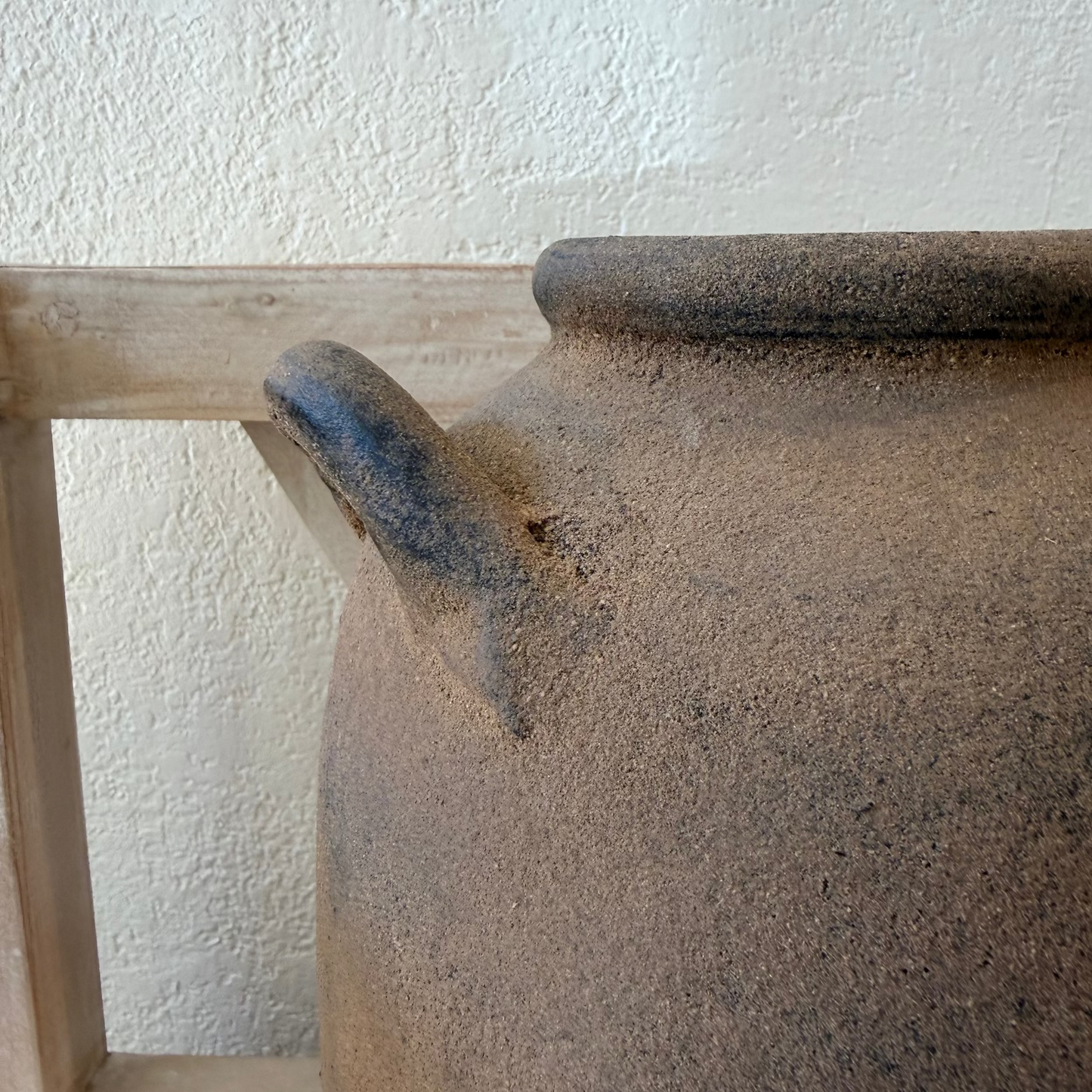 
                  
                    Brown ceramic pot with a wooden shelf against a white wall
                  
                
