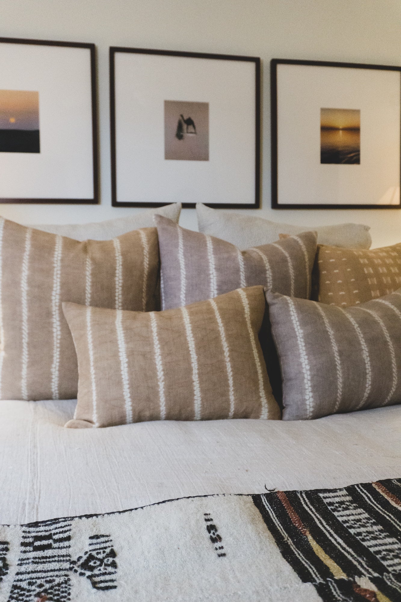 Artisan made, Shibori dyed (Japanese tie-dye) pillows are arranged on a bed. The linen pillows feature a stripe pattern which is made by sewing the pillows prior to hand dying them. They are shown in sand and neutral gray color.