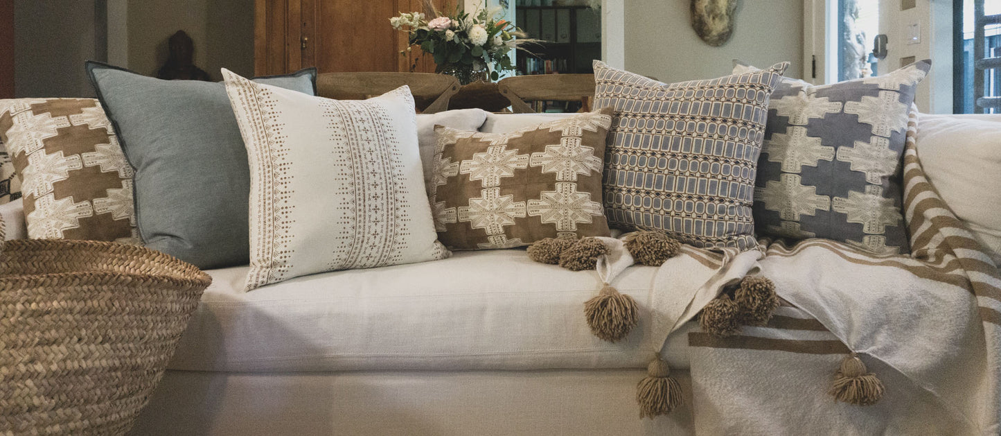 Hand block printed throw pillows on a white couch paired with an oversized pom pom blanket. The artisan made decorative pillows feature hand stamped patterns in earthy browns and blues.