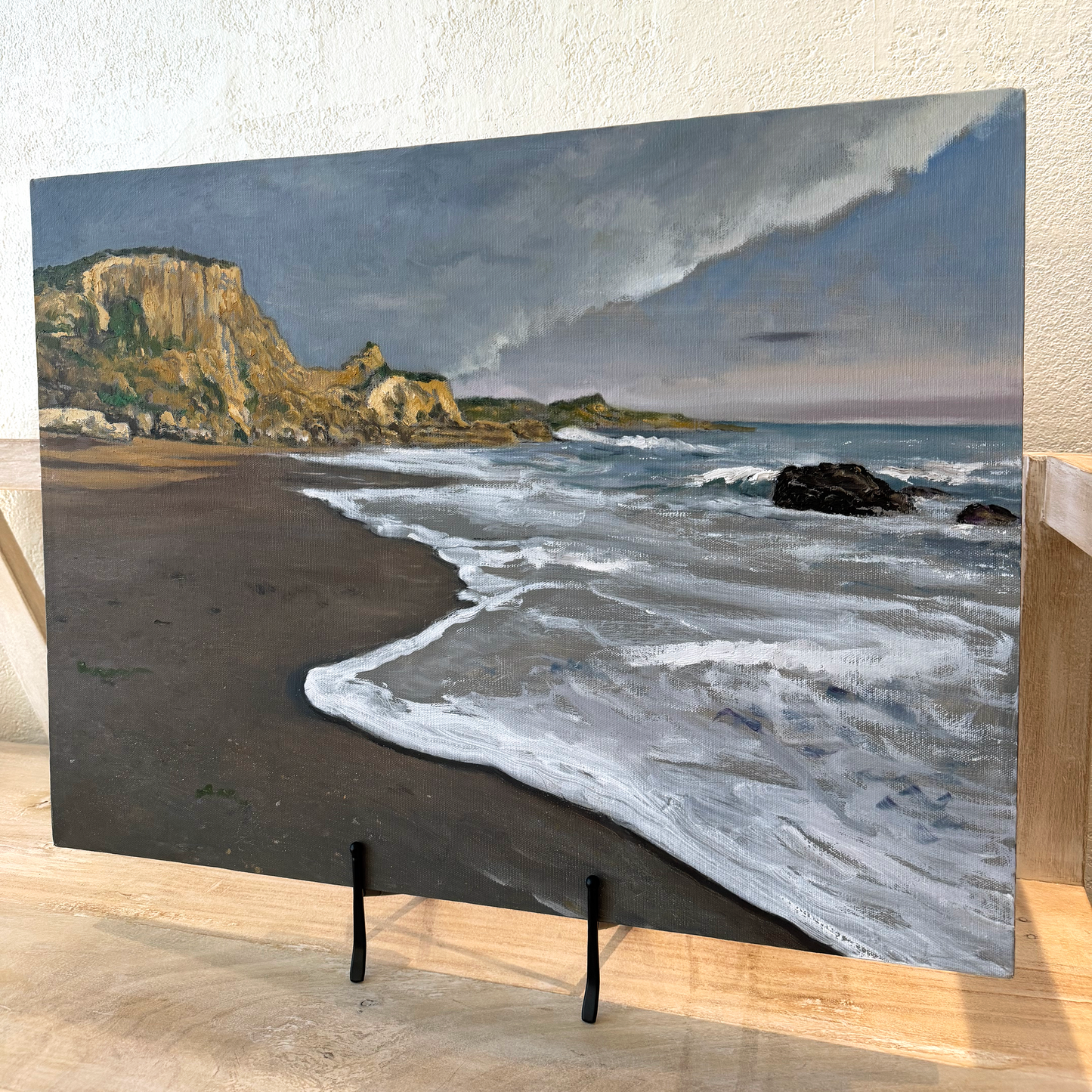 Beach scene with waves and cliffs on a stand against a textured wall.