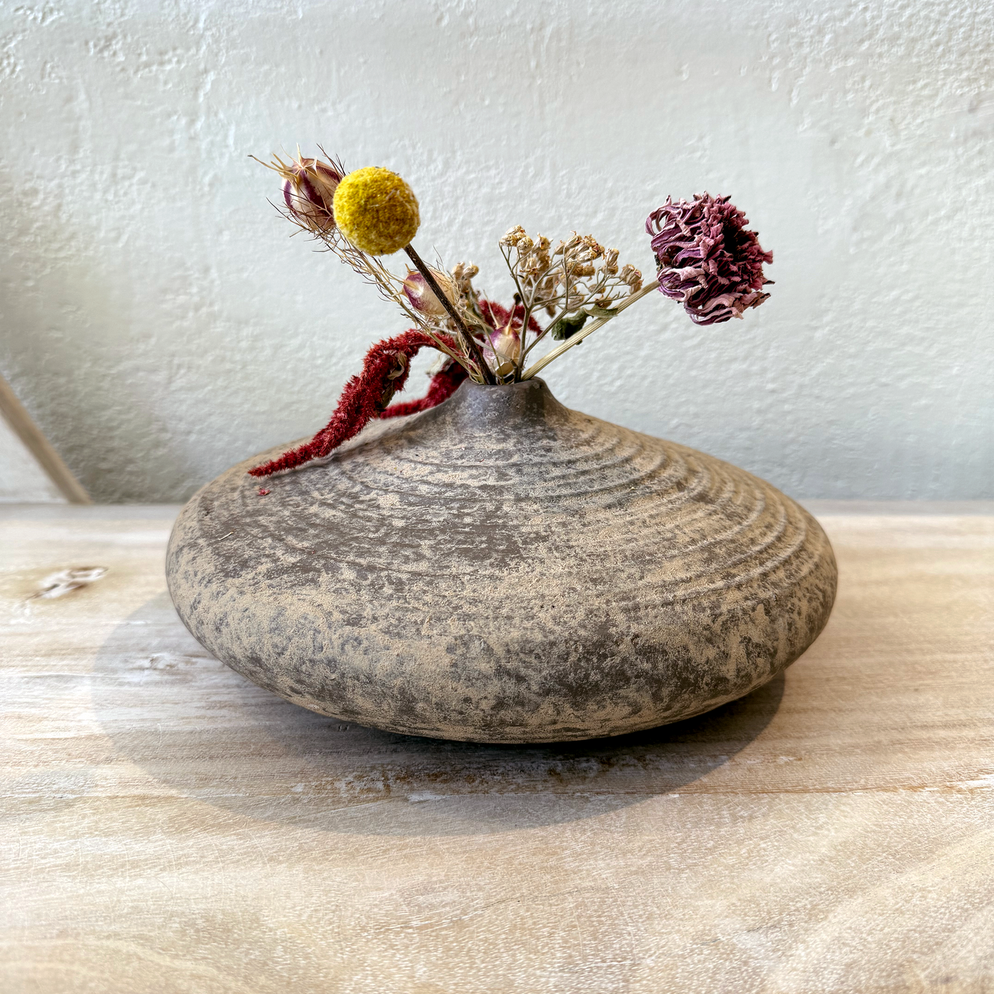 Stoneware vase with dried flowers on a wooden surface
