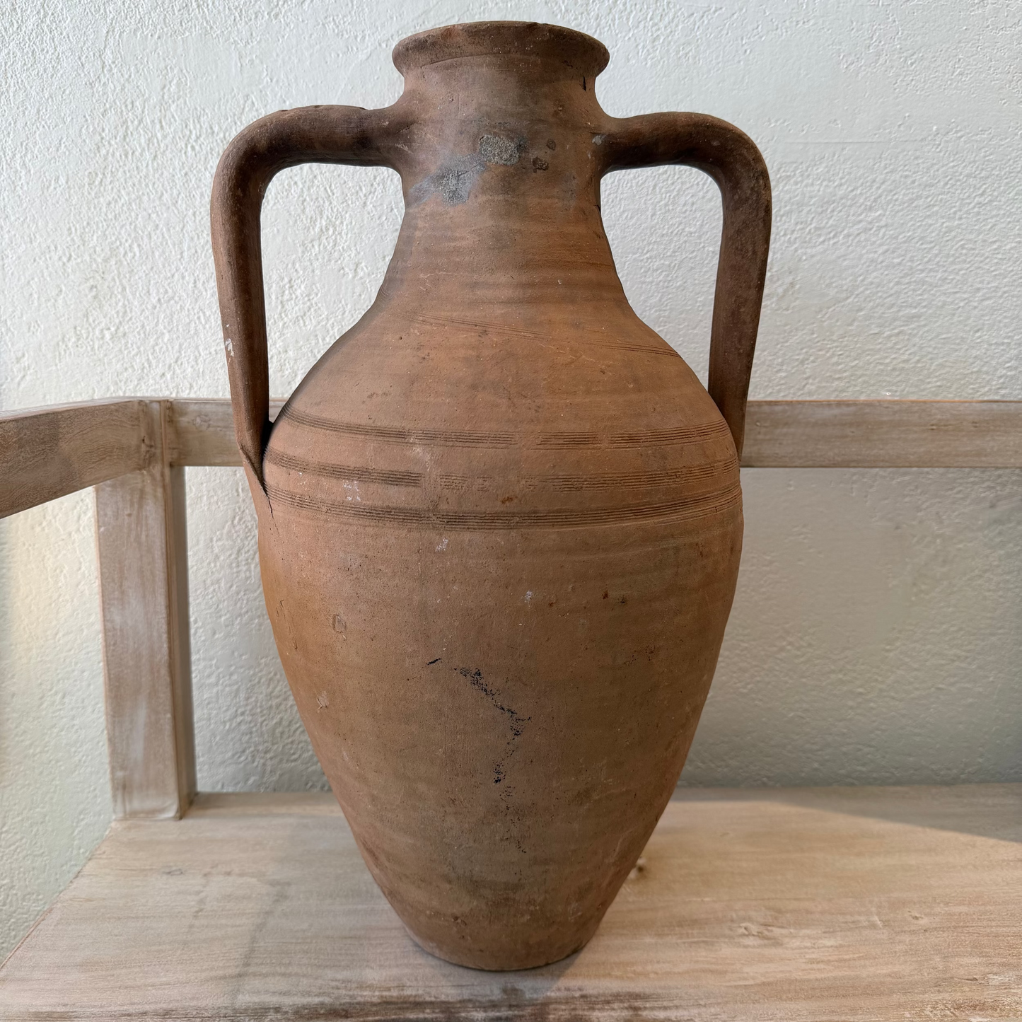 Brown ceramic vase with handles on a wooden surface against a light wall.