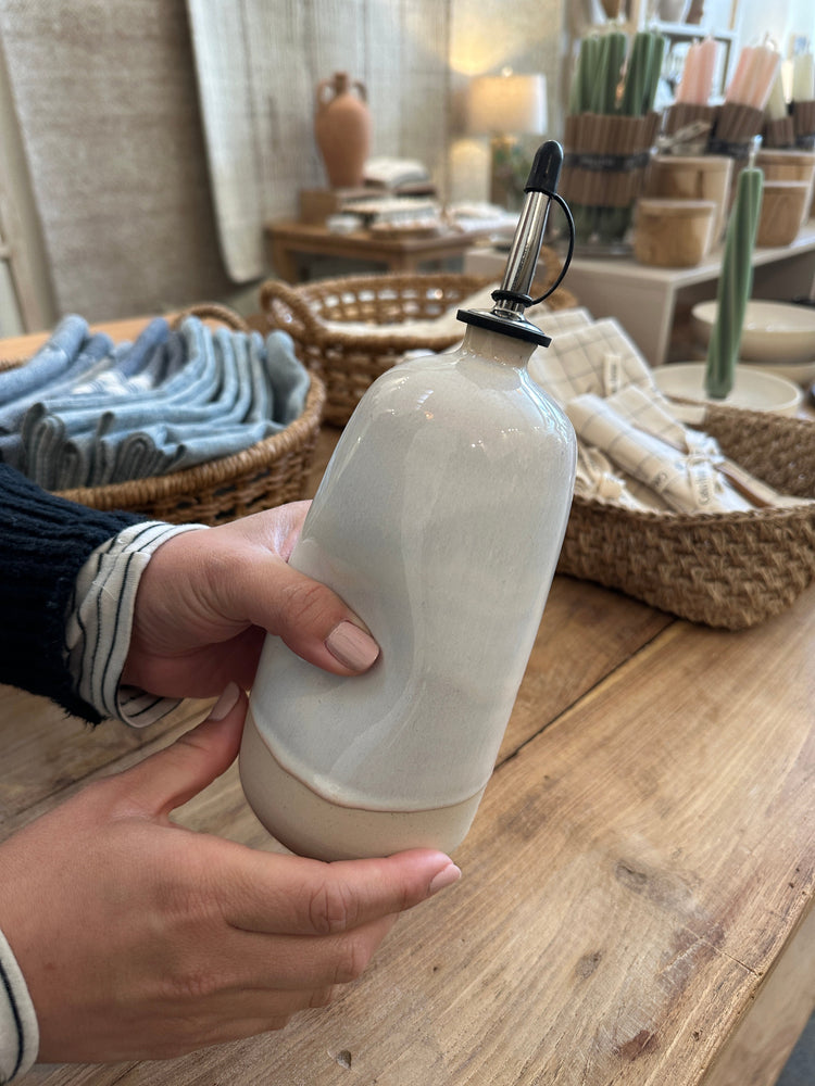 
                  
                    A close up of a hand holding a tall olive oil dispenser
                  
                