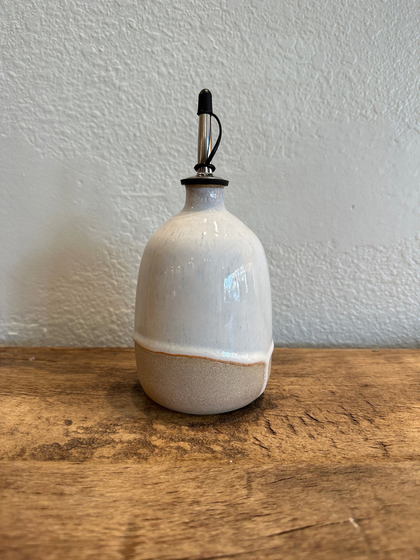 an in store photo of a short olive oil dispenser on a wooden surface and white background