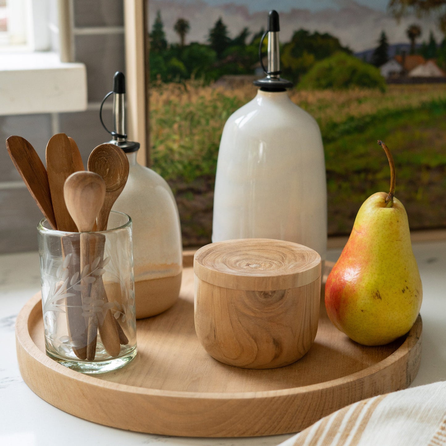A kitchen setting with a landscape painting in the background and an olive oil dispenser in the foreground 