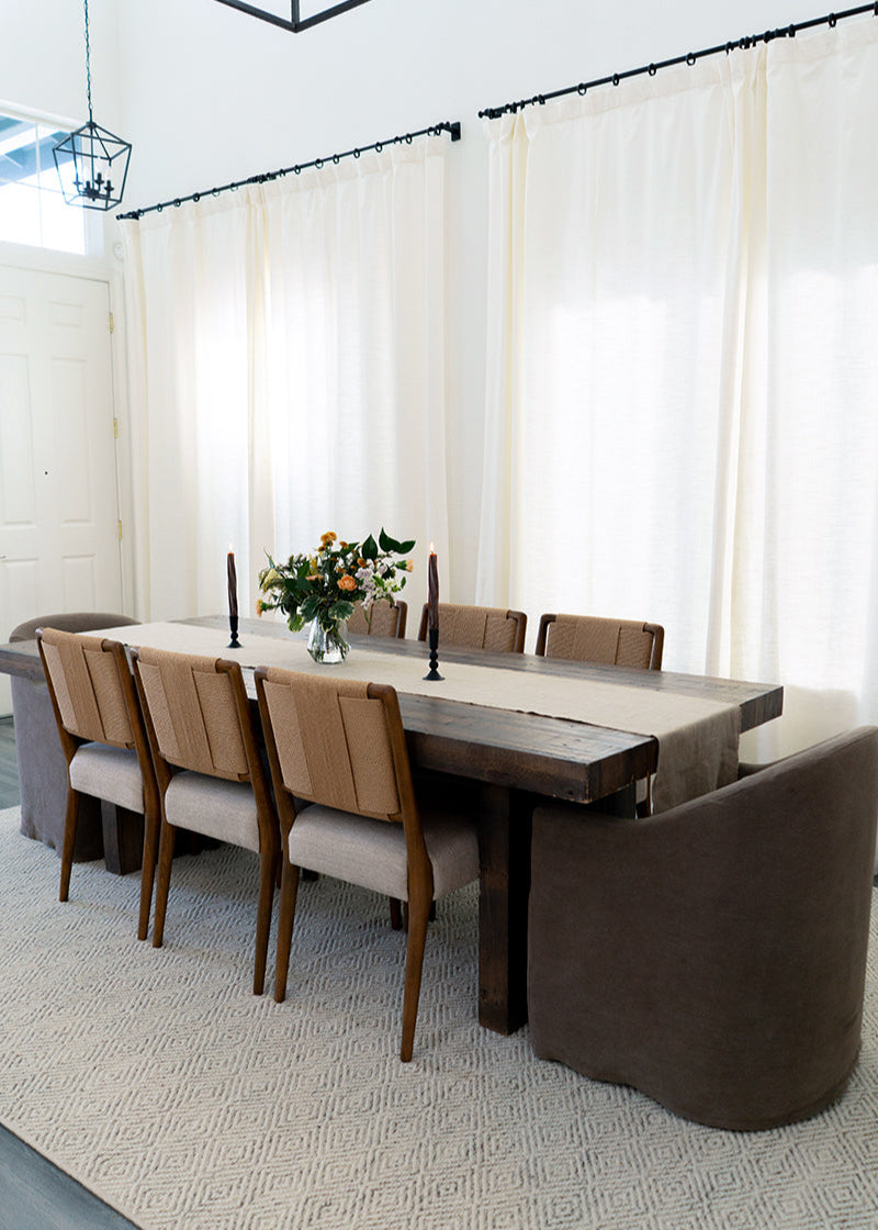 Dining room with a long wooden table and chairs, featuring a vase of flowers.