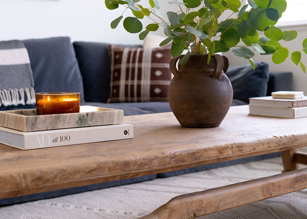 Wooden coffee table with a vase, books, and candle on a living room setting