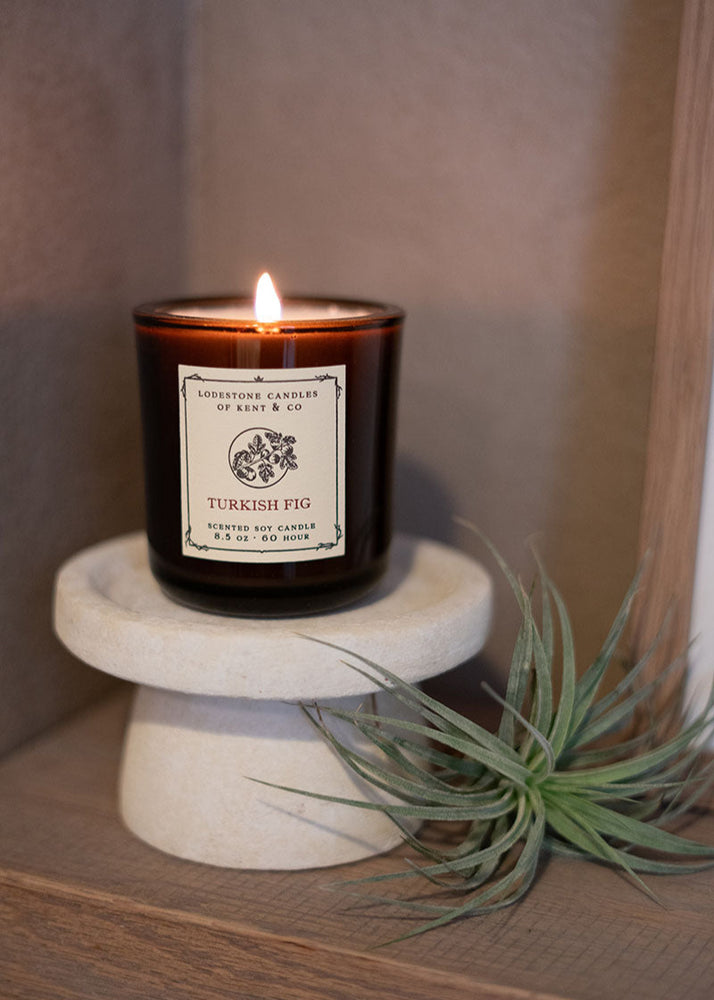Candle with a label on a small marble stand next to an air plant.