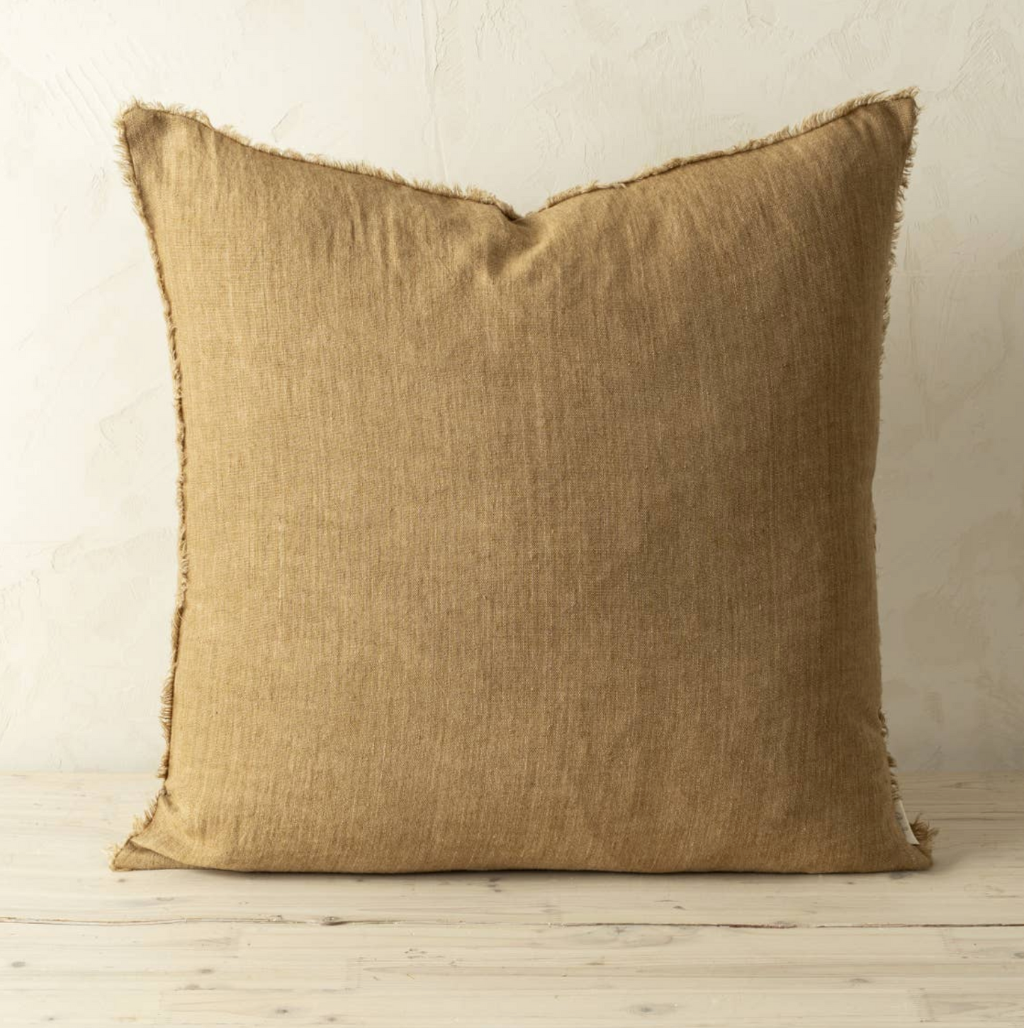 Beige pillow with frayed edges on a wooden floor and light-colored wall background