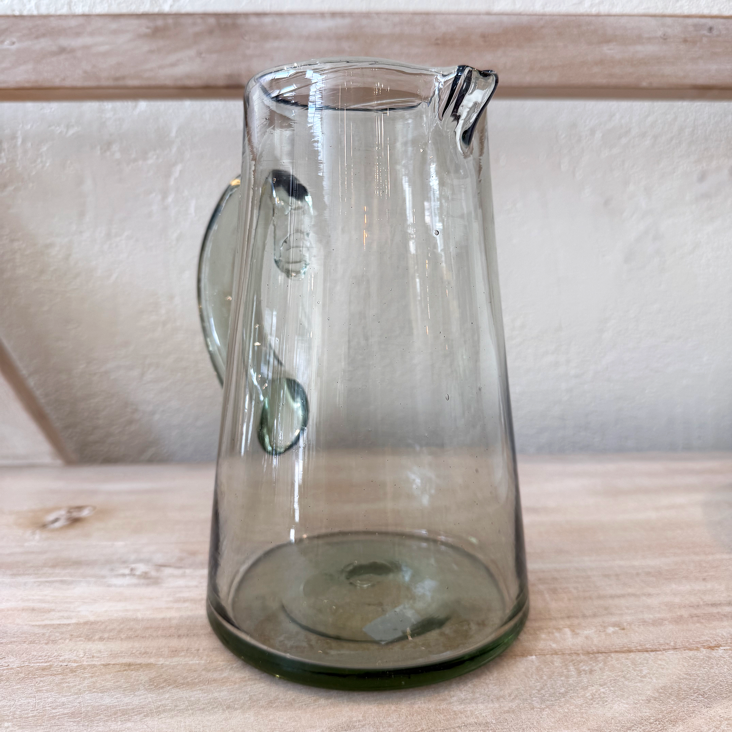 Clear glass pitcher on a wooden surface with a white wall background