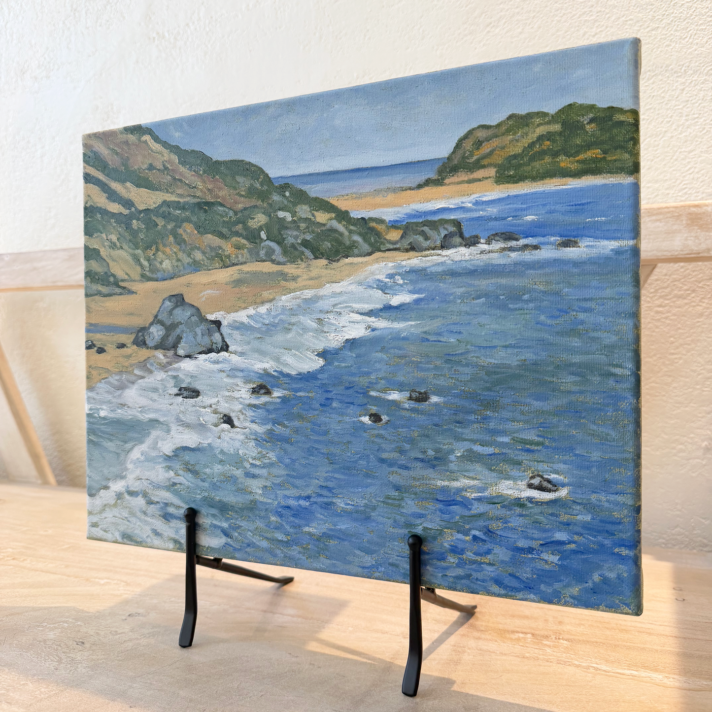 Painting of a coastal scene with a easel on a metal surface