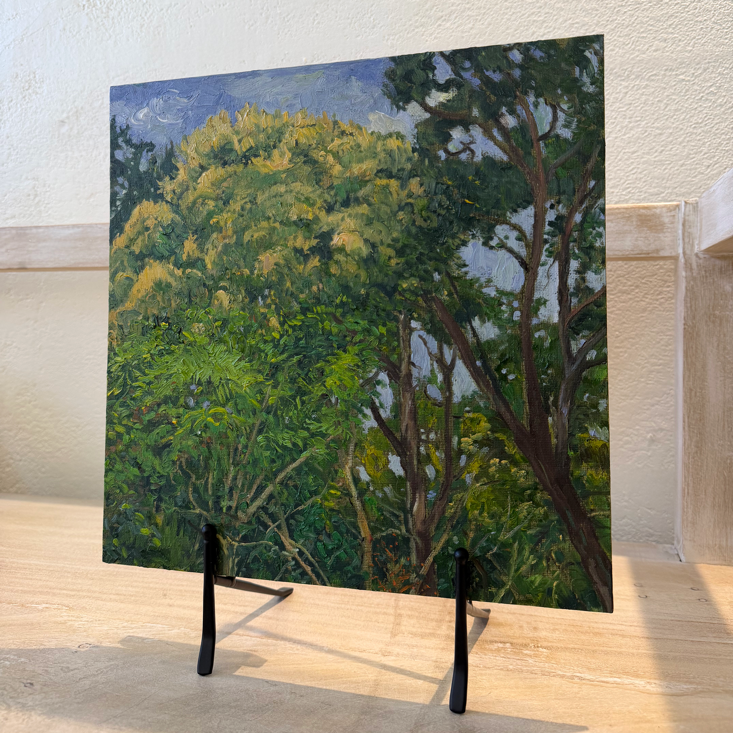 Painting of trees on a stand against a light-colored wall.
