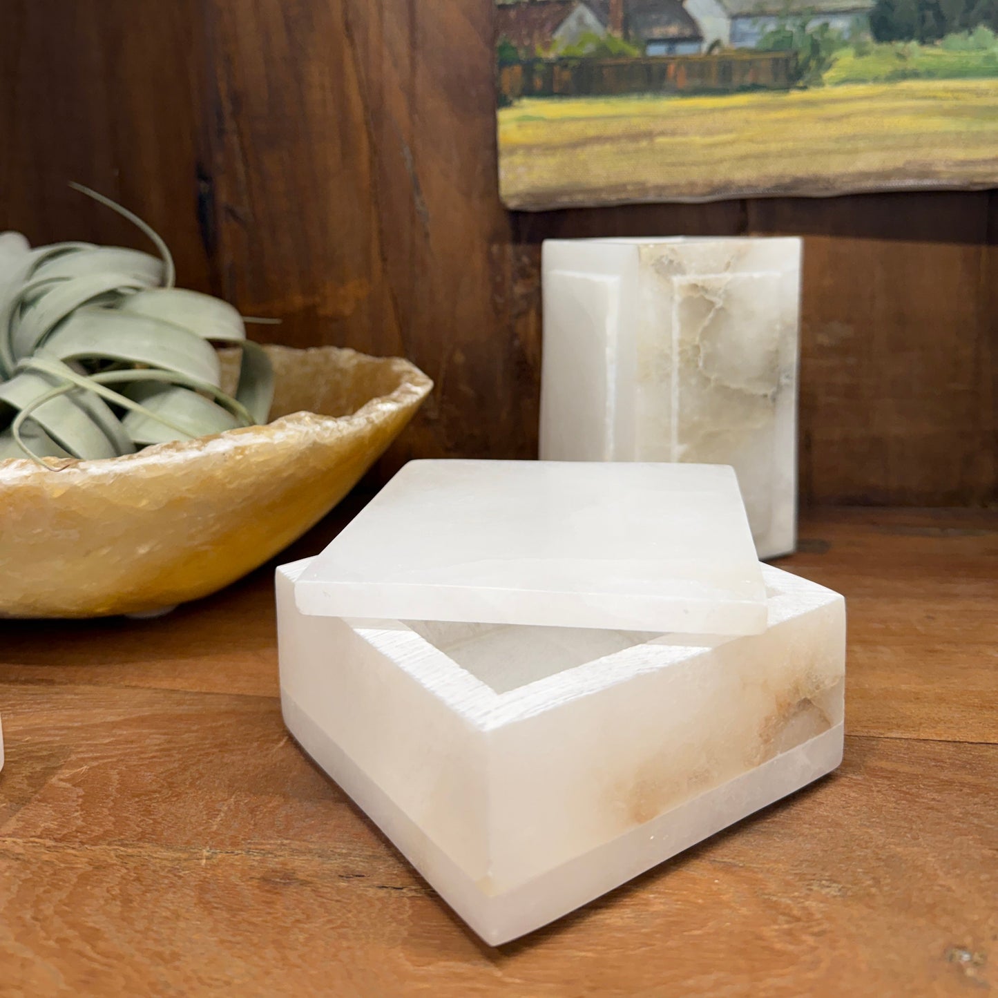 
                  
                    White stone box on a wooden surface with a painting in the background
                  
                