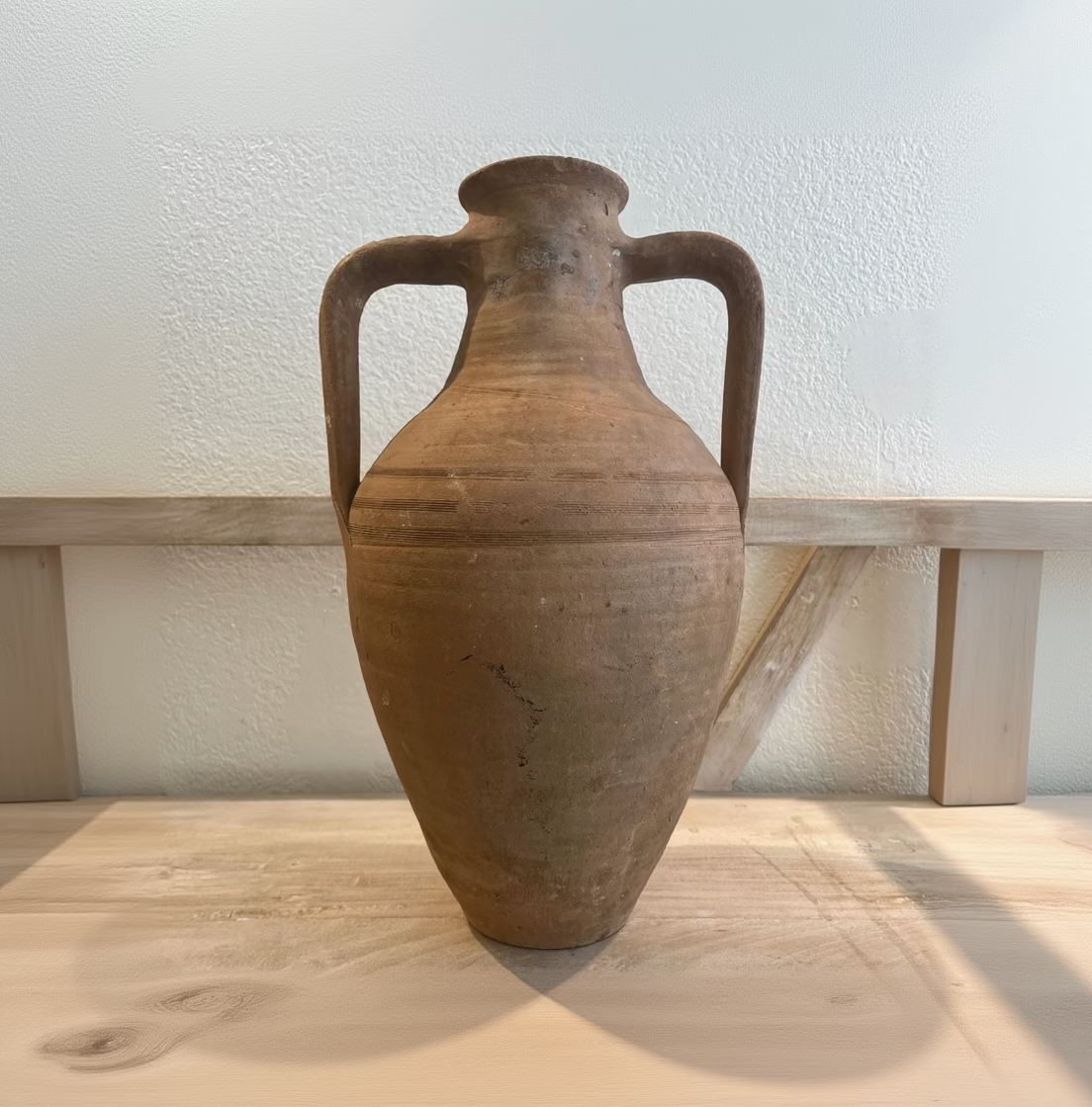 Brown ceramic vase with handles on a wooden surface