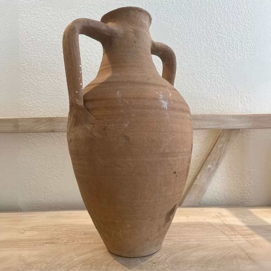 Terracotta vase with handles on a wooden surface and light-colored wall background