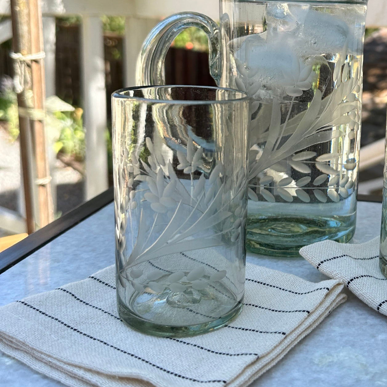 A clear hand-etched drinking glass with a floral motif, displayed on a striped napkin.