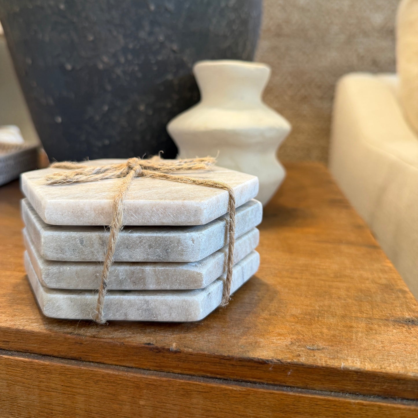 Stack of stone coasters tied with twine on a wooden surface with decorative vases in the background.