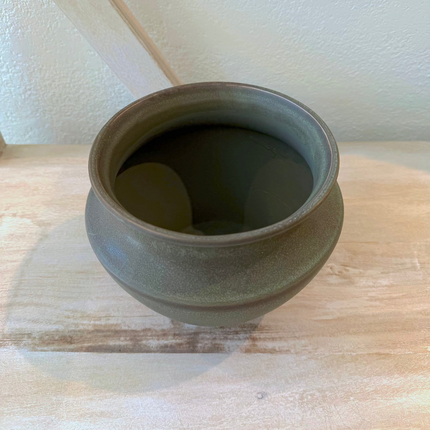 Green ceramic pot on a wooden surface with a white wall background