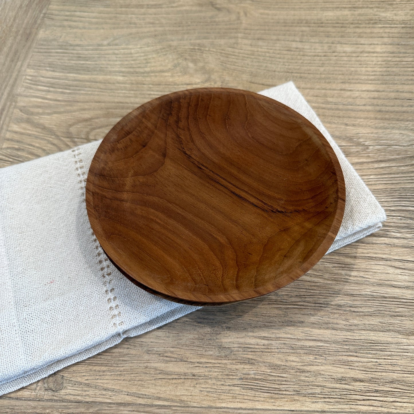 
                  
                    Small teak wood plate on cloth napkin.
                  
                