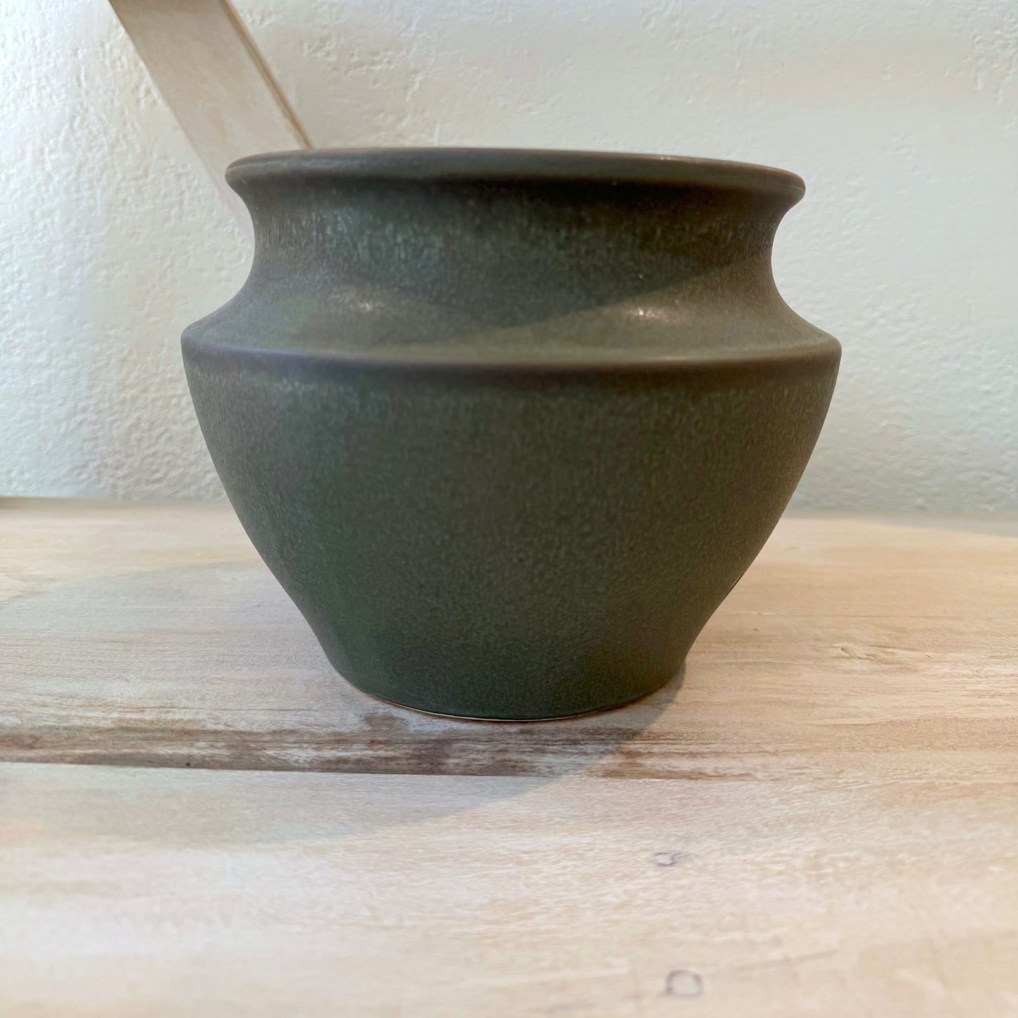 Dark green ceramic vase on a wooden shelf against a white wall