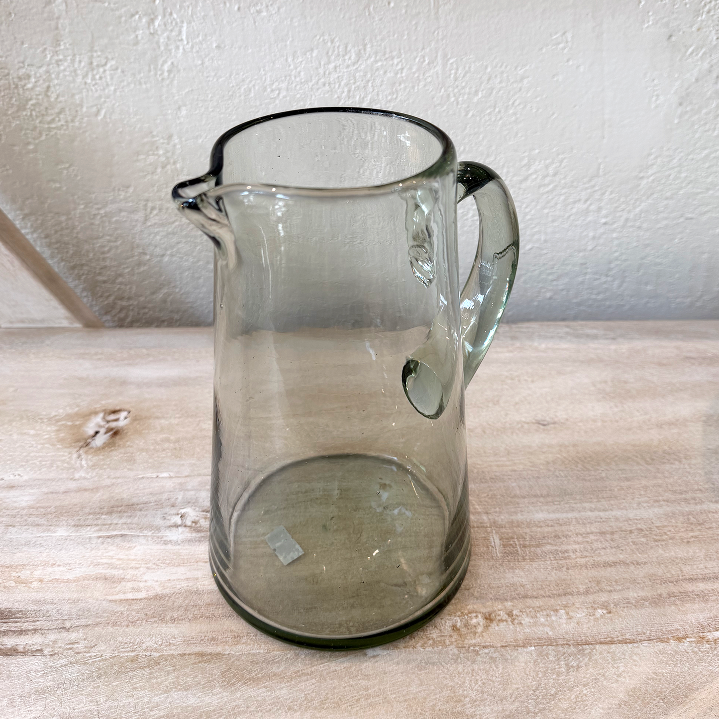 Clear glass pitcher on a wooden surface with a neutral background