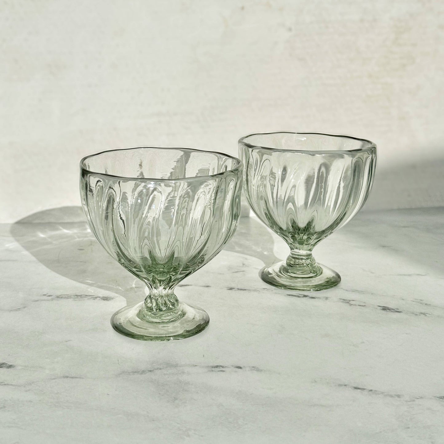 
                  
                    Two clear glass goblets on a marble surface with a light gray background
                  
                