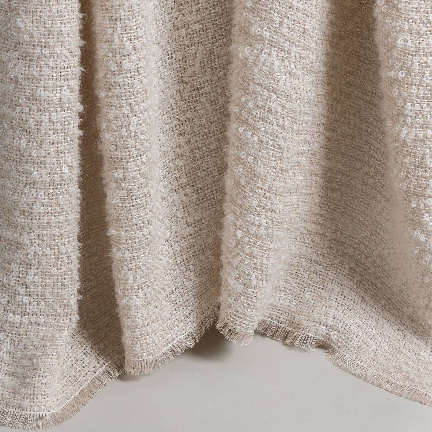 
                  
                    A close-up of draped textured mohair and linen throw blanket in a warm cream or oatmeal tone, showing the woven texture and soft folds against a light neutral background.
                  
                