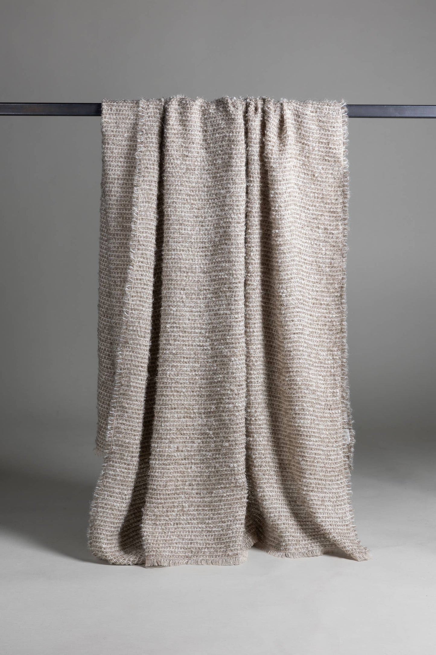 
                  
                    Textured beige  throw blanket draped over a black rod against a gray background
                  
                