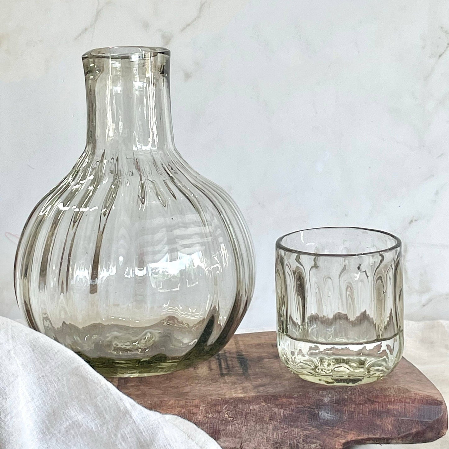 
                  
                    Clear glass carafe and tumbler on a wooden board with a marble background
                  
                