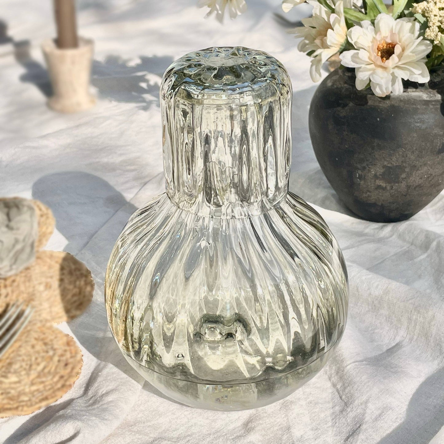 
                  
                    Clear glass vase on a textured surface with flowers in the background
                  
                