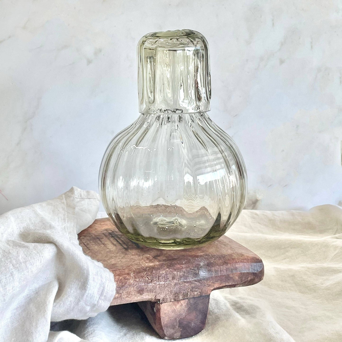 
                  
                    Clear glass bottle on a wooden stand with a white cloth and marble background
                  
                