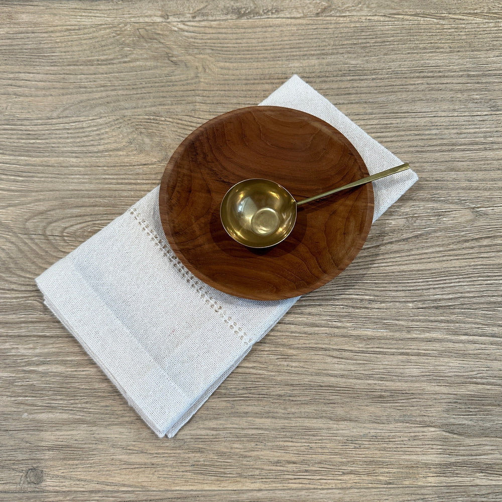 Brass spoon on small teak plate and cloth napkin.