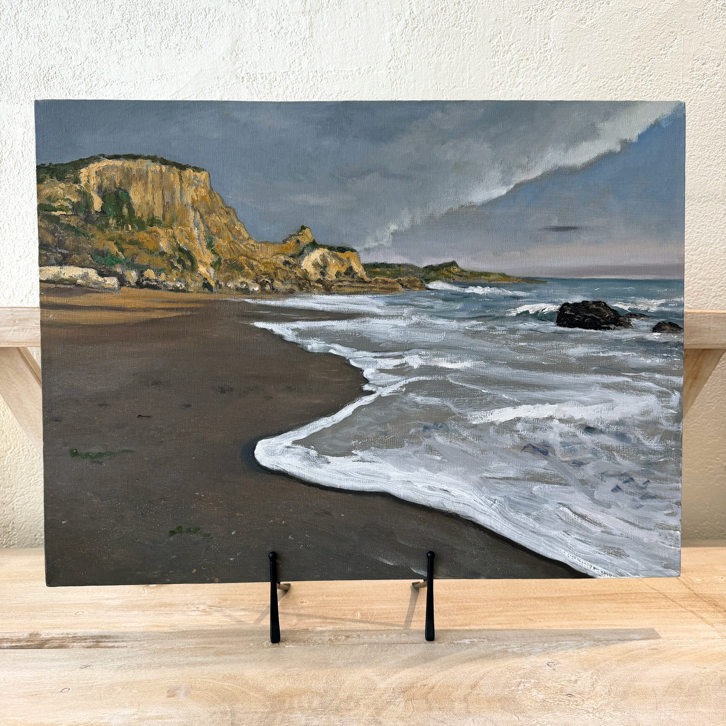 Canvas print of a coastal scene with waves and cliffs on a wooden surface.