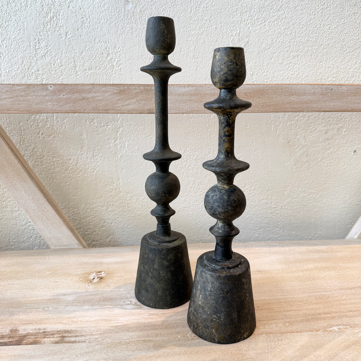 Two black and green metal candle holders on a wooden surface with a light-colored wall background.