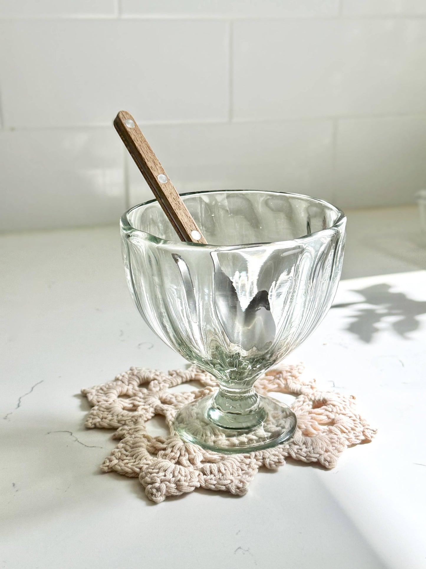 
                  
                    Clear glass bowl with a wooden spoon on a white surface with a crochet doily
                  
                