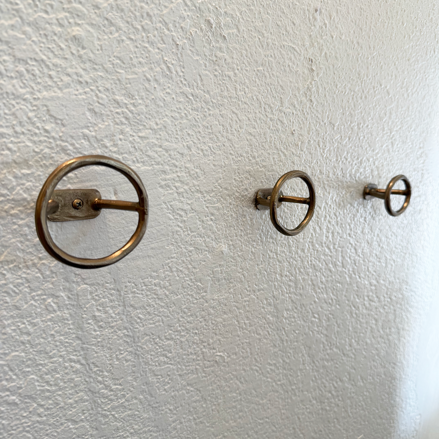 Three brass wall hooks on a textured white wall