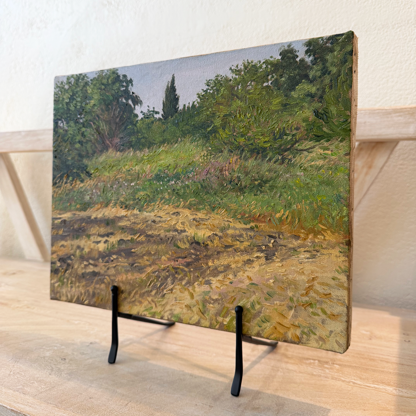 Framed artwork of a landscape on a wooden stand against a white wall.
