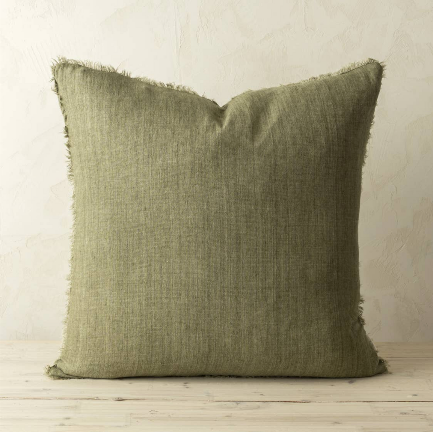 
                  
                    Green pillow with frayed edges on a wooden surface and light background
                  
                