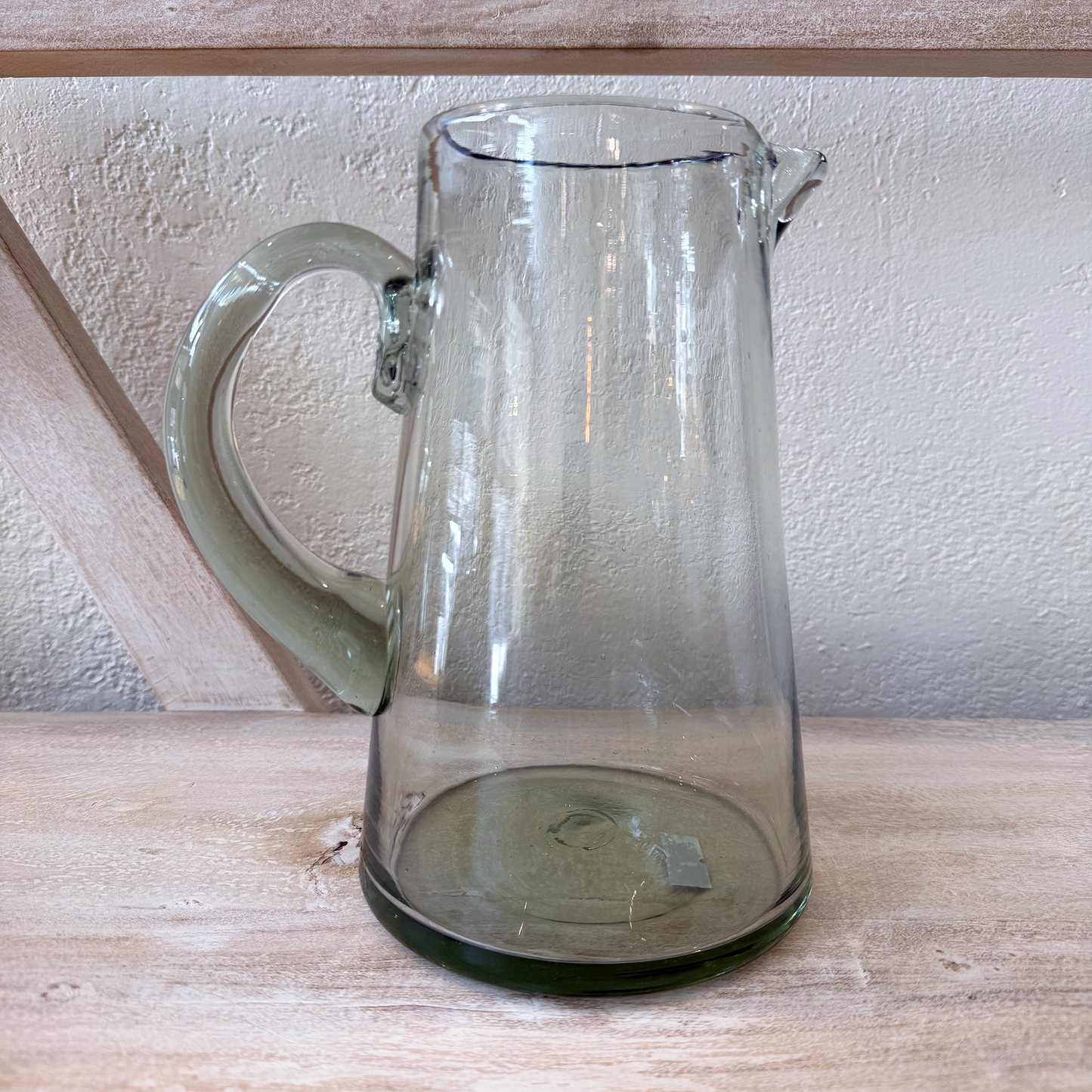 
                  
                    Clear glass pitcher on a wooden surface with a neutral background
                  
                