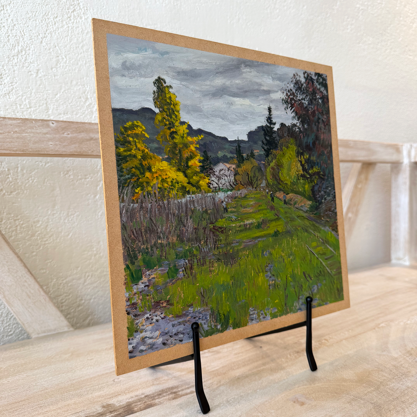Framed landscape painting on a stand against a textured wall.