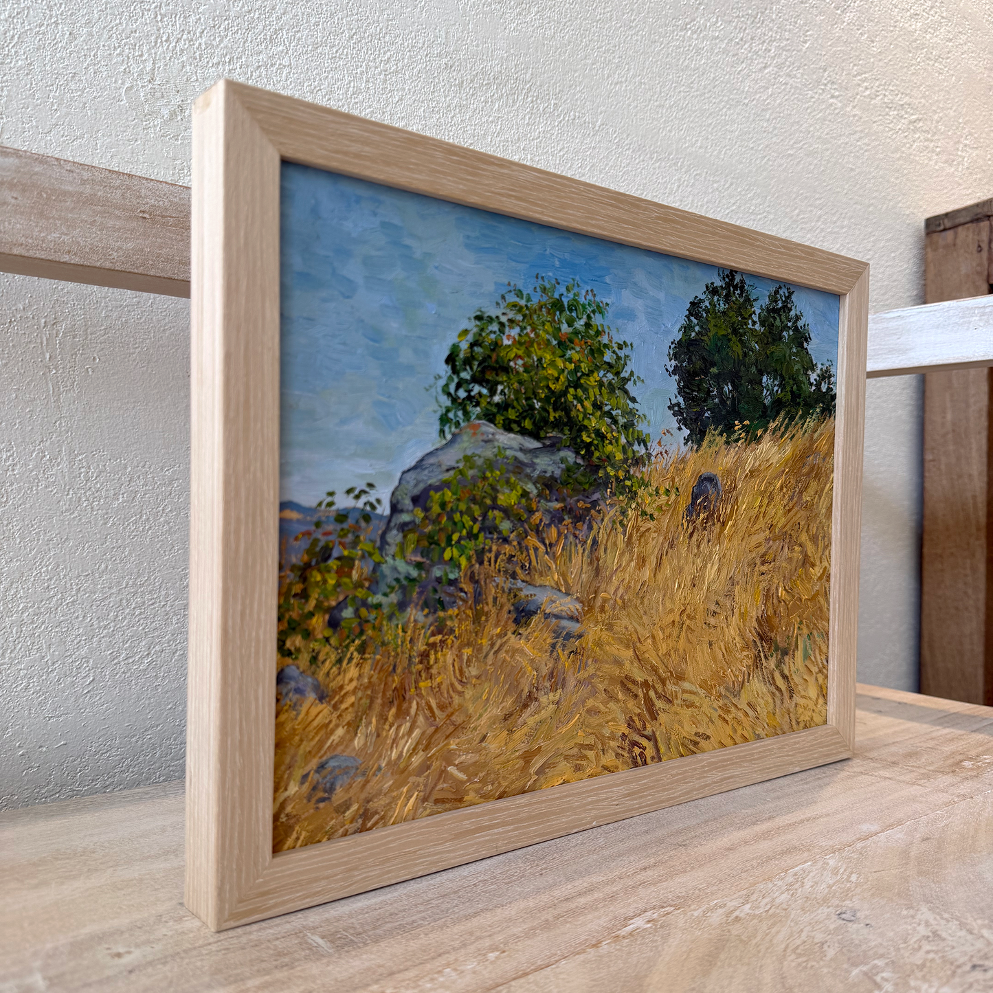 Framed painting of a natural landscape with trees and grass on a wooden surface.